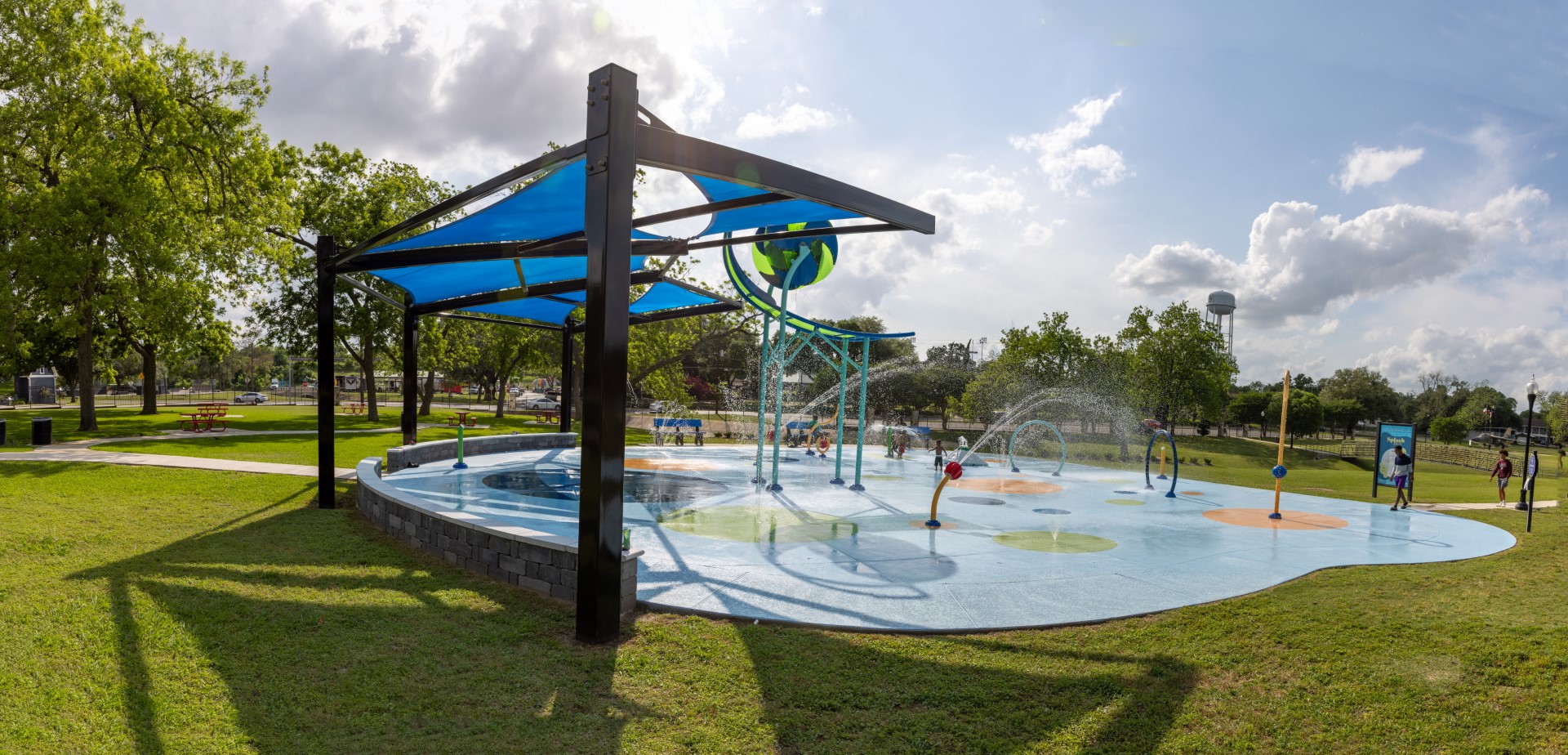 Splash pad on a sunny day with a shade structure over the seating area.
