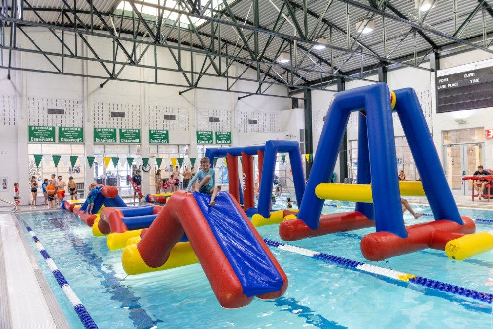 Large Inflatable play structures floating in an indoor pool with children playing on top of them