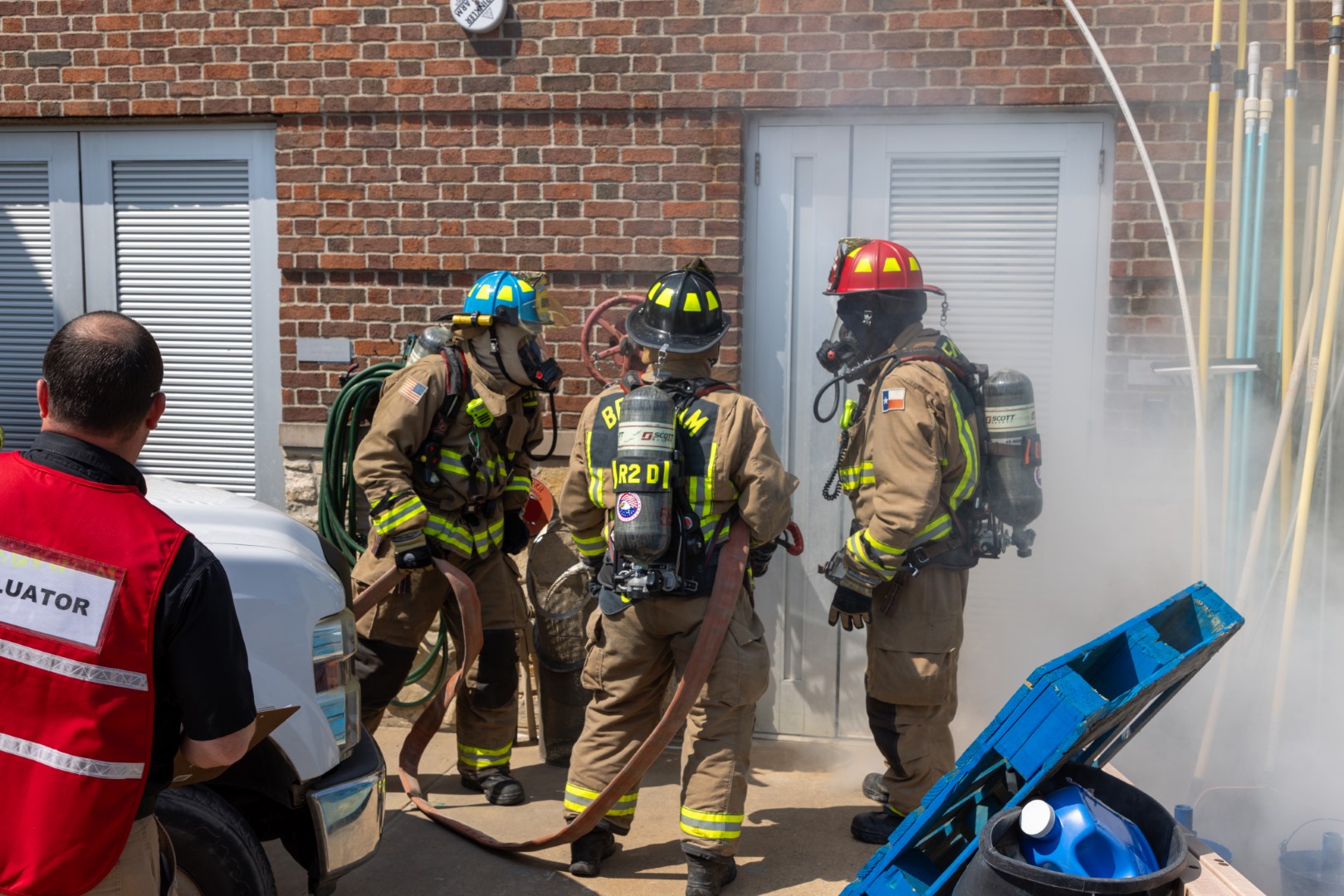 firefighters preparing to enter a building while being evaluated during a drill
