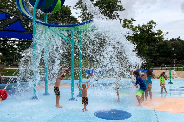 kids getting splashed by the superwave dropping lots of water on top of them at the splashpad at henderson park